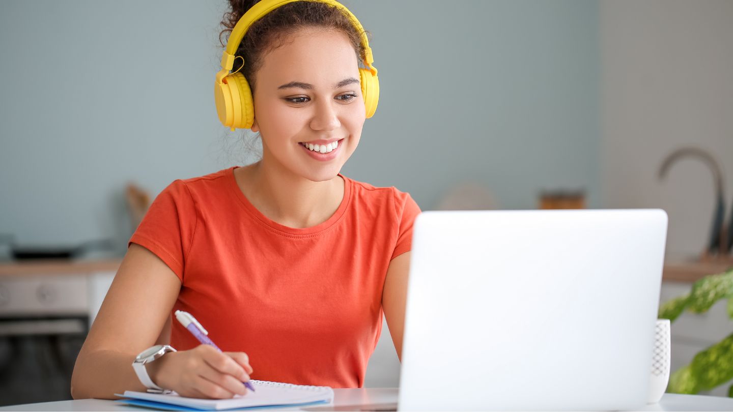 Woman Wearing Headphones Taking Notes During Online Class